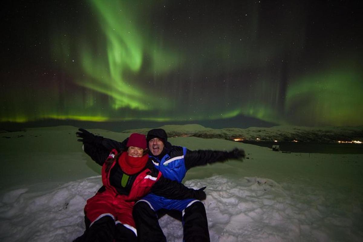 due persone sedute nella neve sotto l'aurora boreale