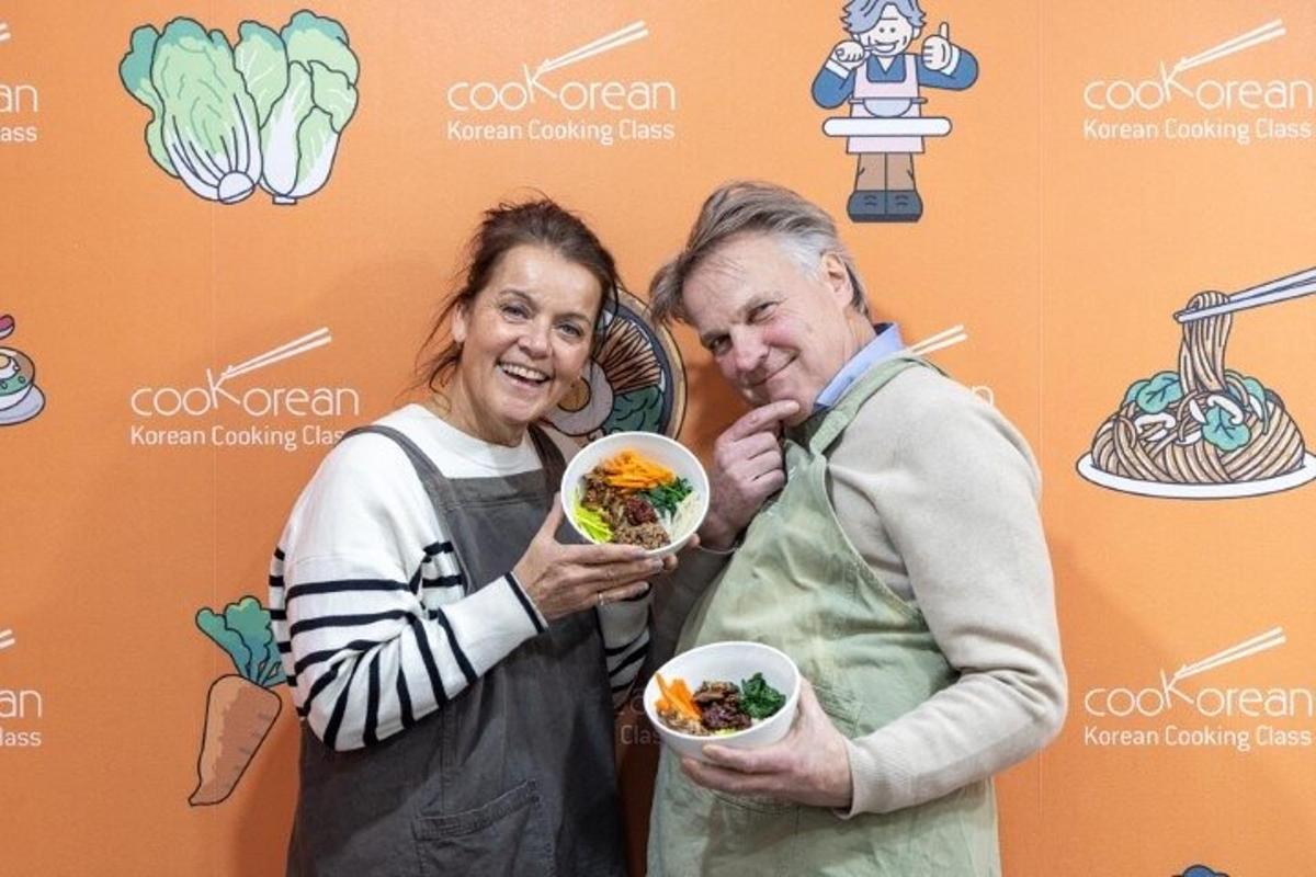 two older women holding bowls of food in front of a wall