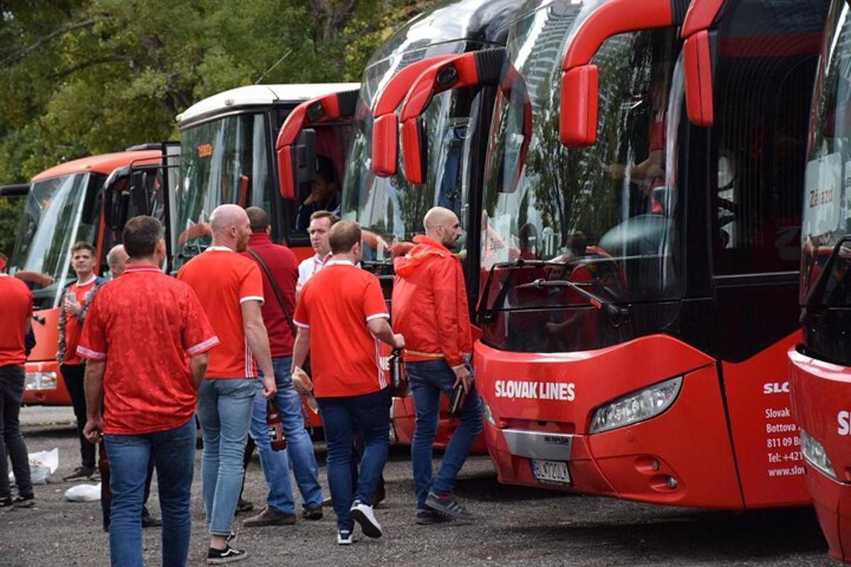Egy csoport piros inges férfi áll a buszok előtt