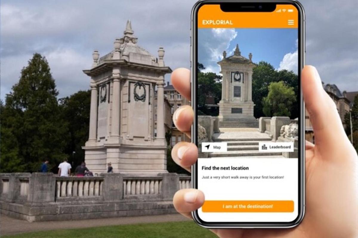 eine Person, die vor einem Denkmal ein Mobiltelefon hochhält