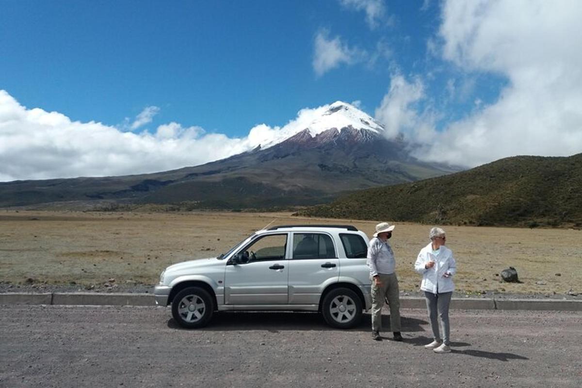 two people standing next to a car in front of a mountain