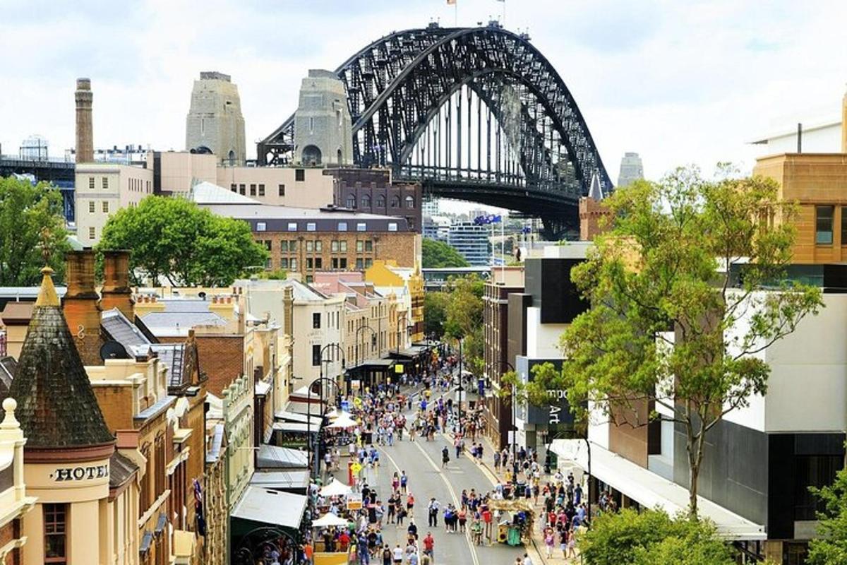 a crowd of people walking down a street in front of a bridge