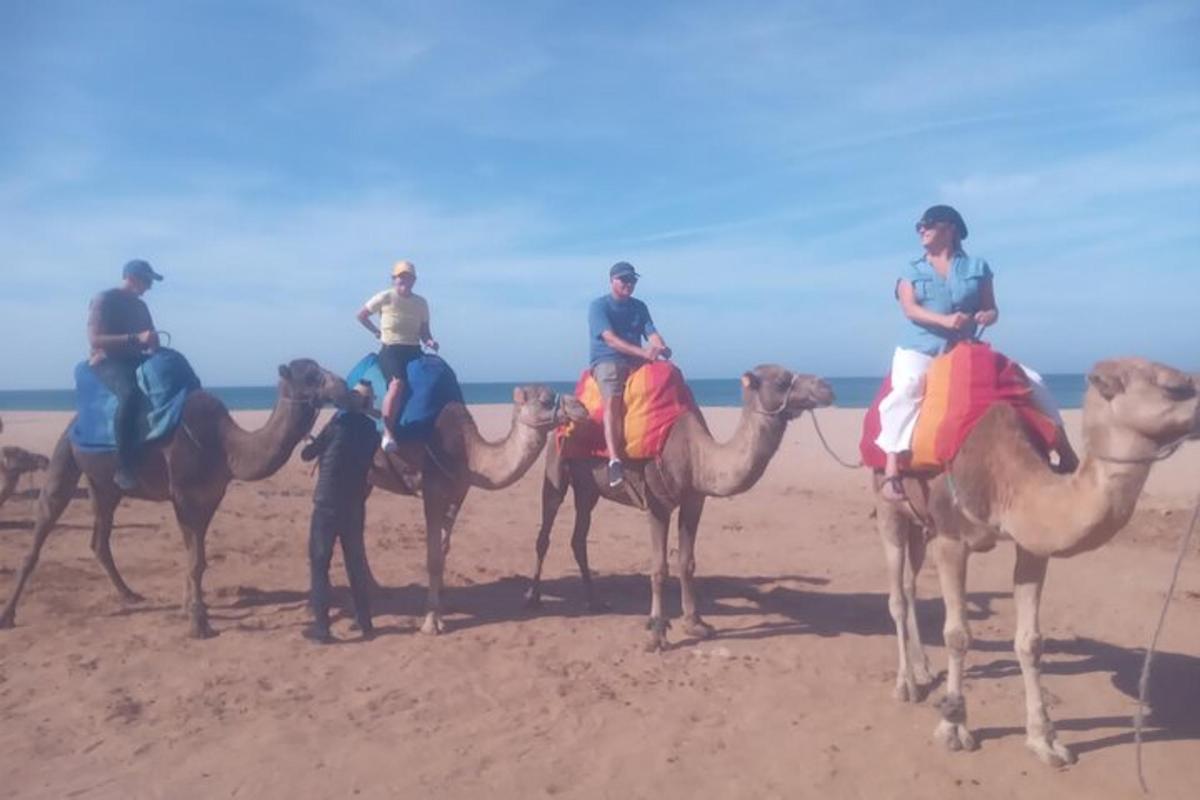 Grupa ludzi jadąca na wielbłądach po plaży