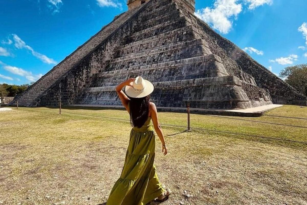 a woman in a dress and hat standing in front of a pyramid