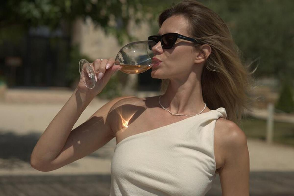 Una mujer con gafas de sol bebiendo una copa de vino.