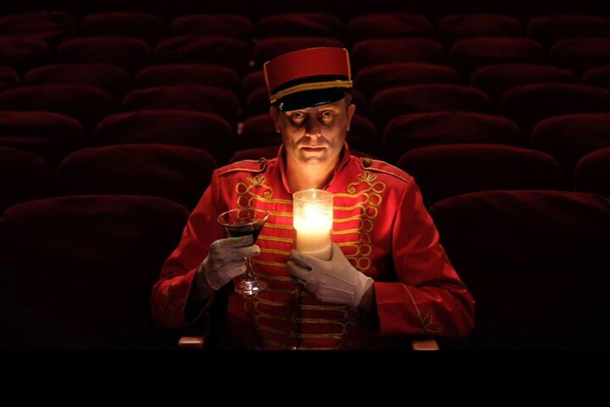 un uomo che tiene in mano una candela e un bicchiere in un auditorium