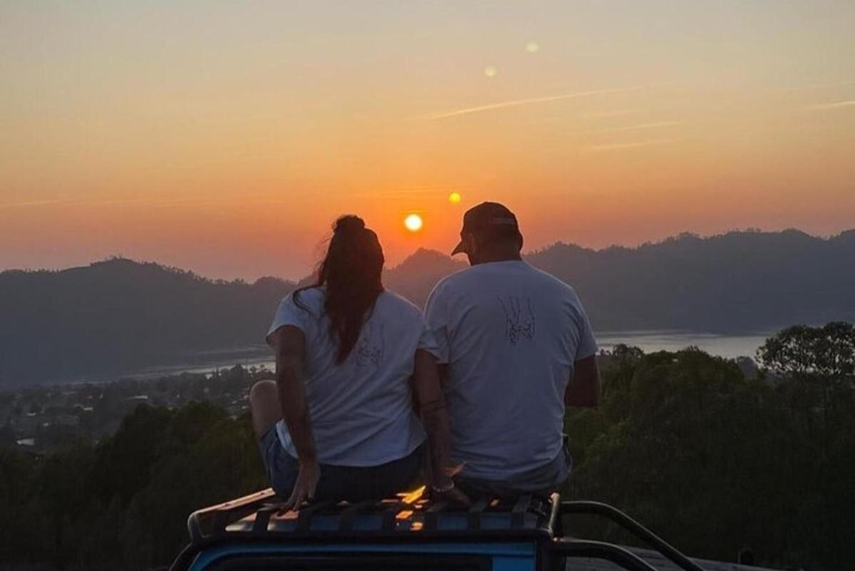 un uomo e una donna seduti in cima a una montagna che guardano il tramonto