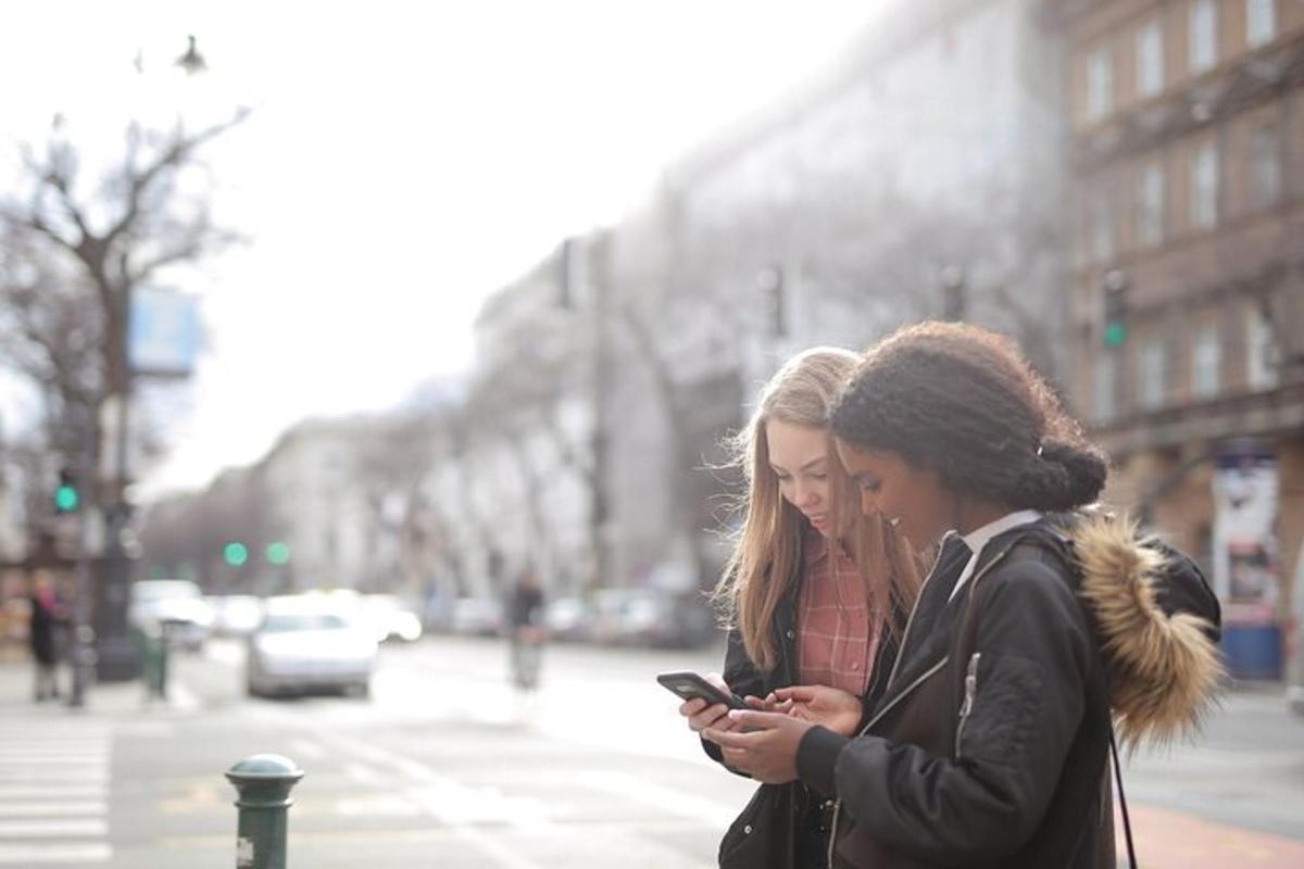 două femei care se uită la un telefon mobil pe o stradă a orașului
