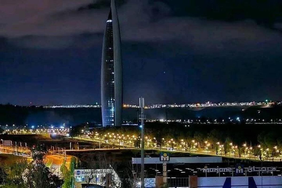 um edifício alto à noite com uma ponte e postes de luz