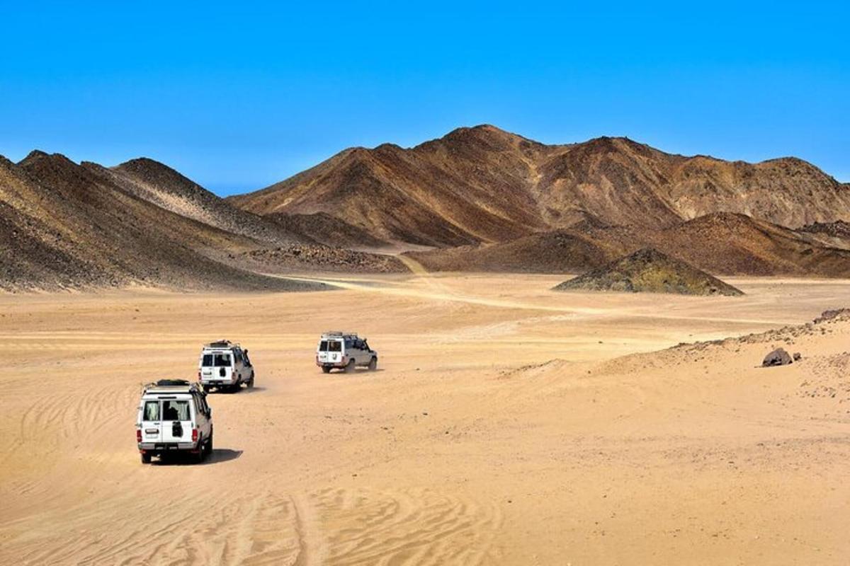 tres vehicles aparcats en un desert amb muntanyes al fons