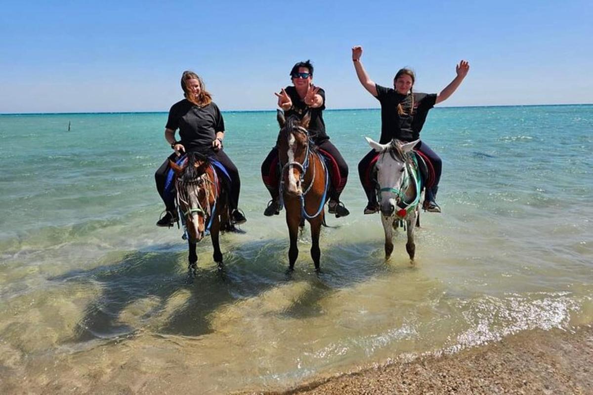 tiga orang menunggang kuda di air di pantai