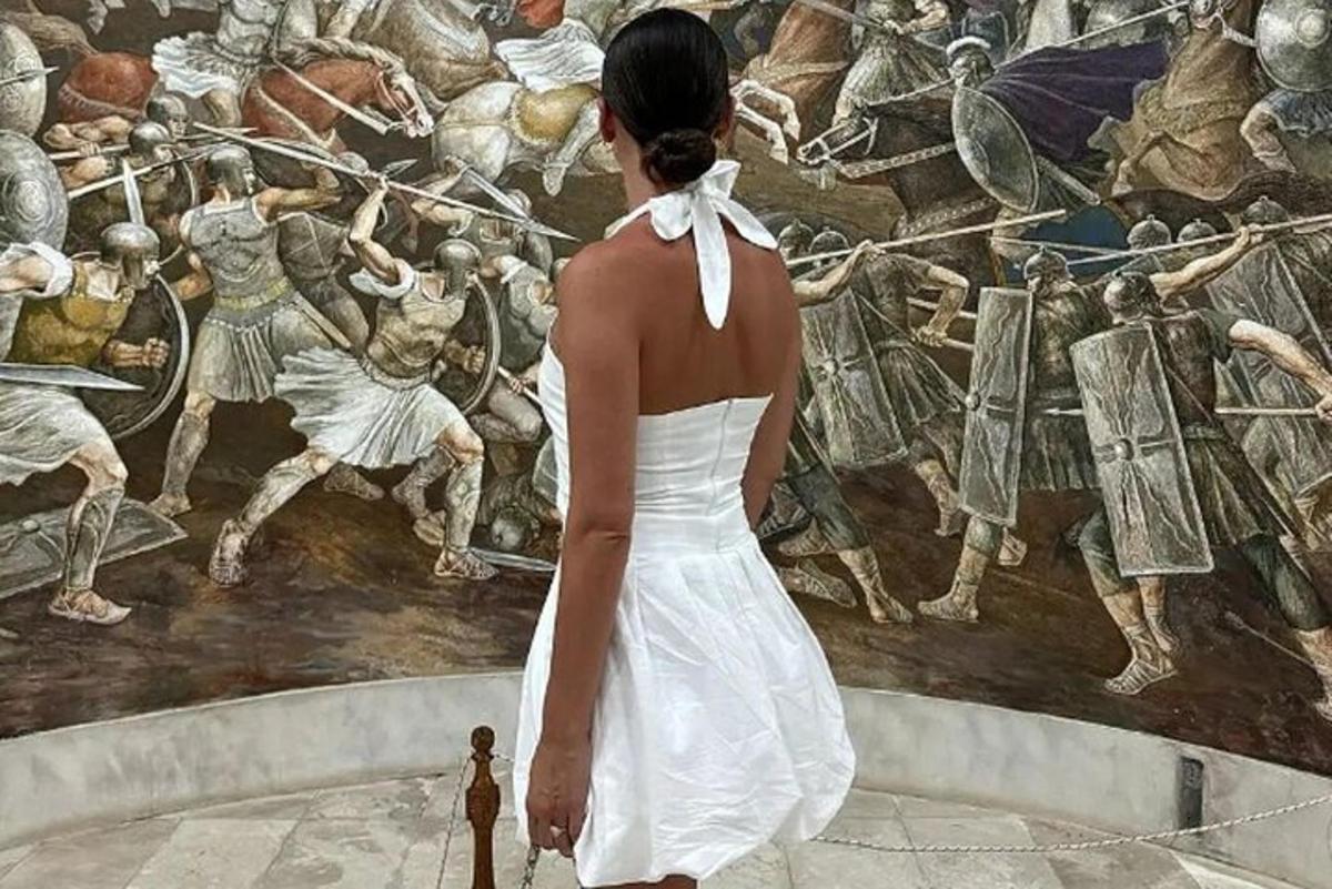 Una mujer con un vestido blanco parada frente a un cuadro.