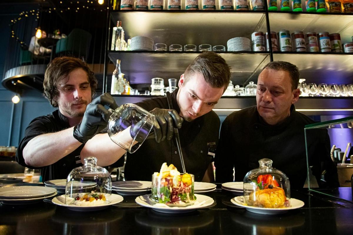 tre uomini in piedi dietro un bar che preparano il cibo