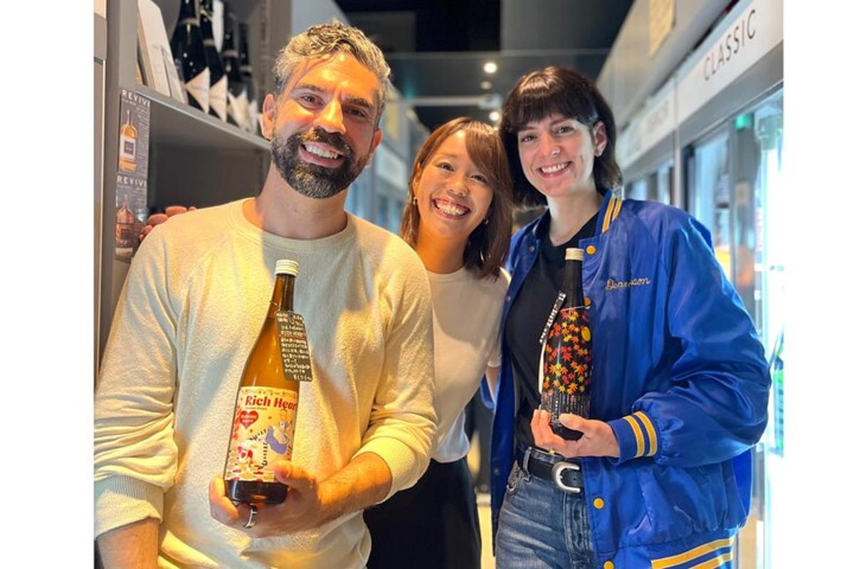 zwei Frauen und ein Mann halten eine Flasche Wein