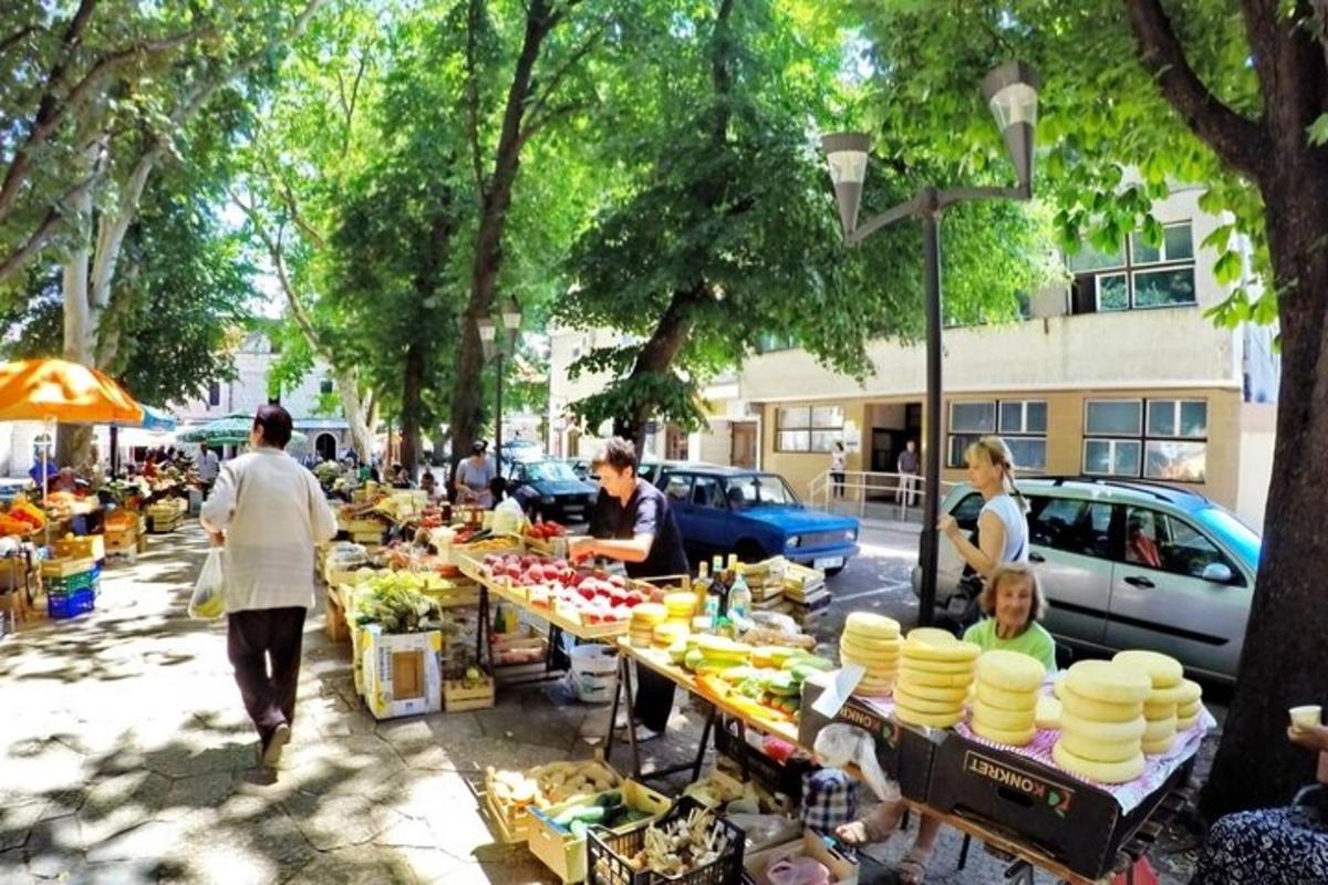 a group of people walking past a market with tables filled with food