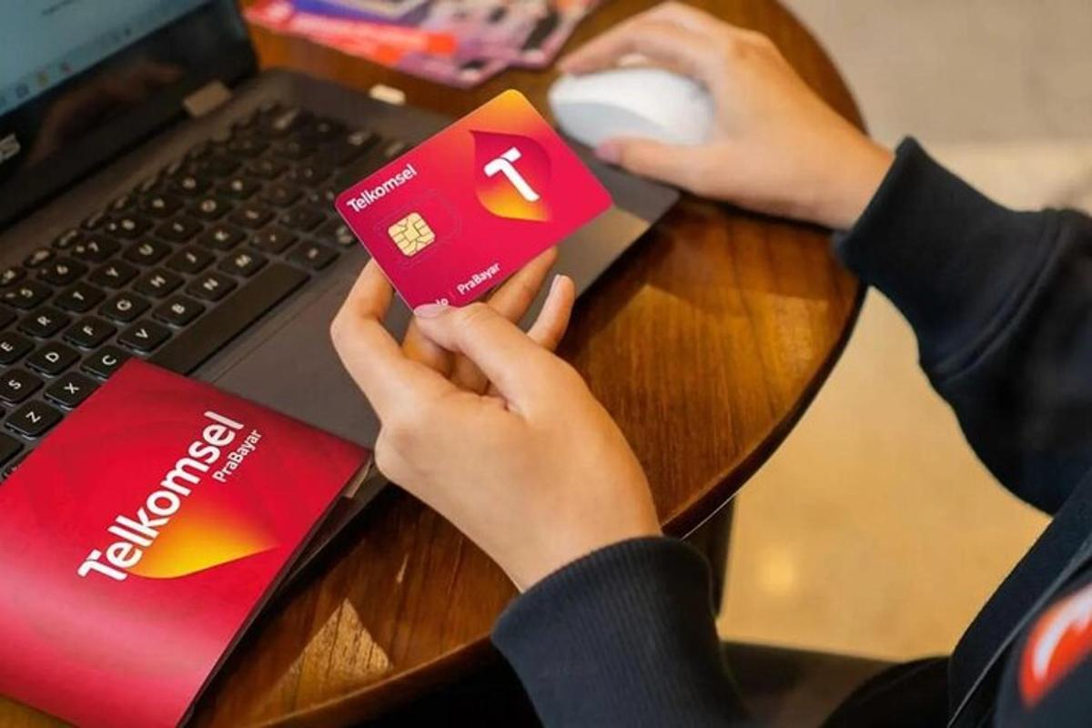 una persona seduta a una scrivania con un computer portatile e una persona che tiene in mano una carta di credito