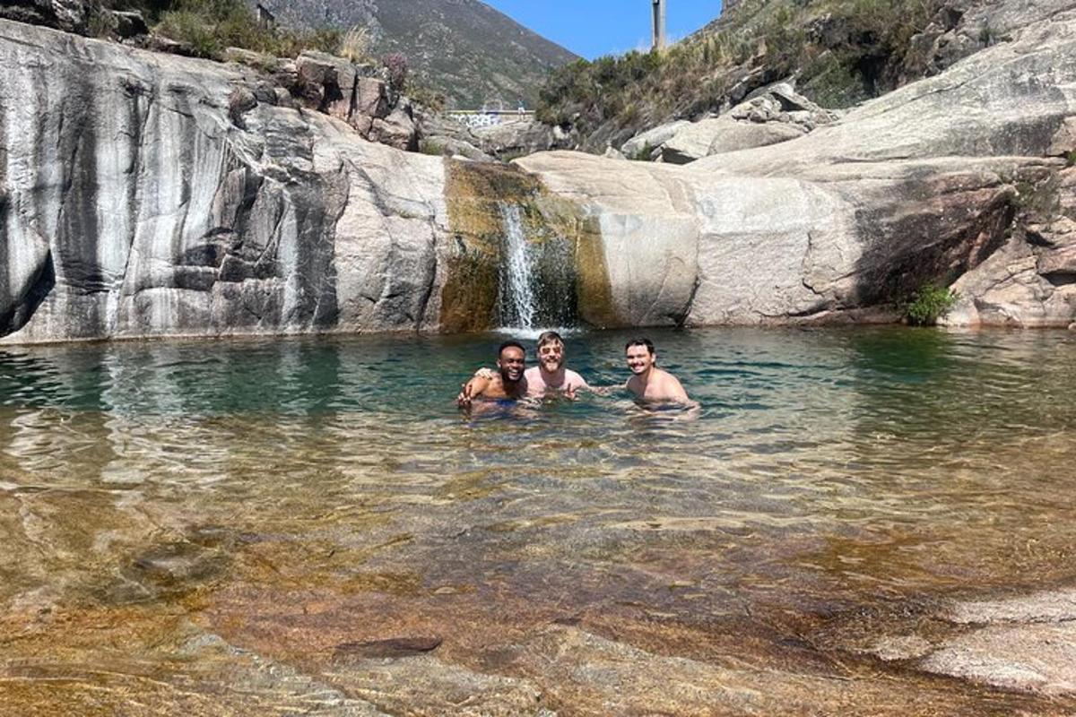 drei Personen schwimmen in einem Fluss mit Wasserfall