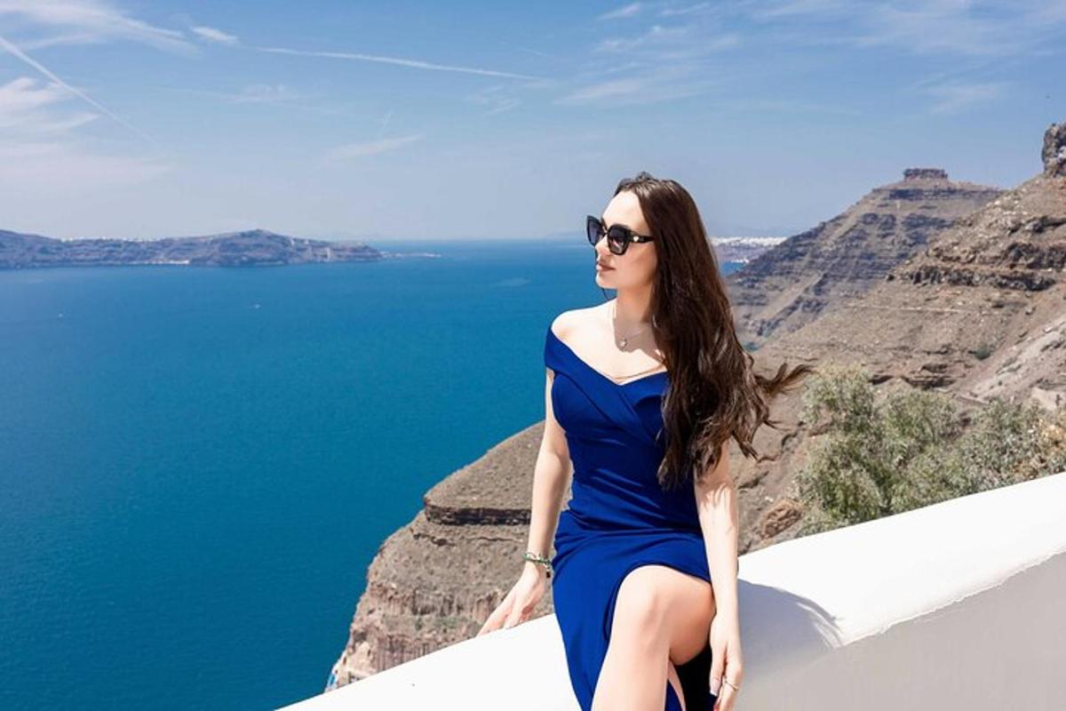 žena v modrých šatech sedící na římse s výhledem na vodu
