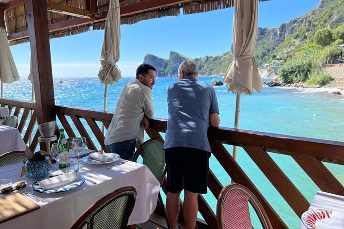 two men standing on a balcony looking out at the ocean