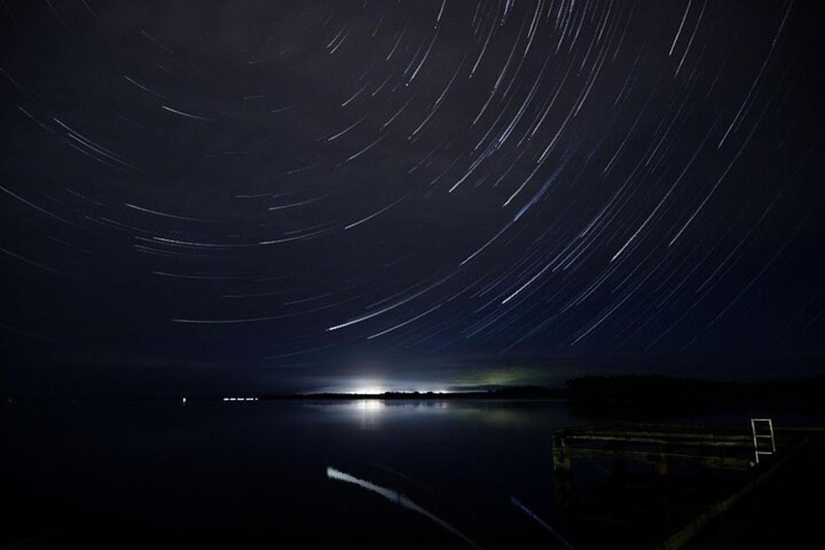 una scia di stelle nel cielo notturno sopra uno specchio d'acqua