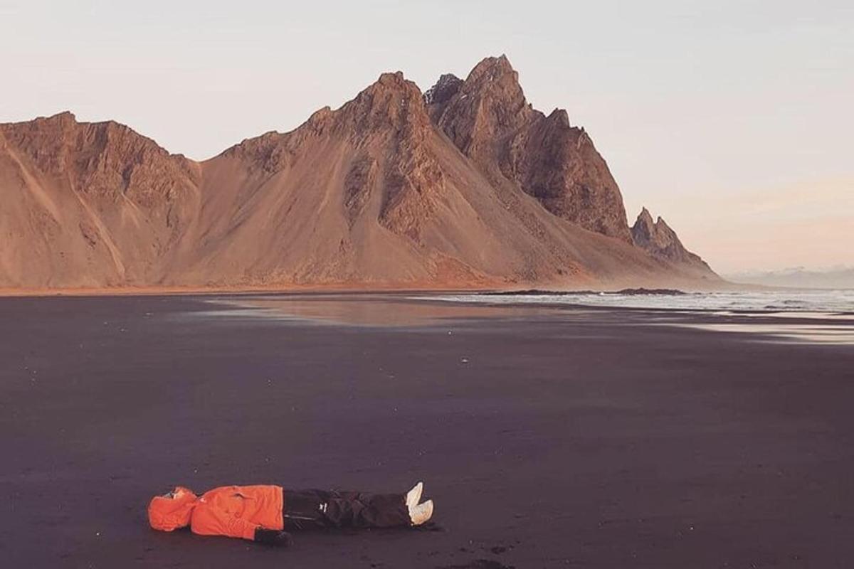 Una persona tumbada en una playa con una montaña al fondo.