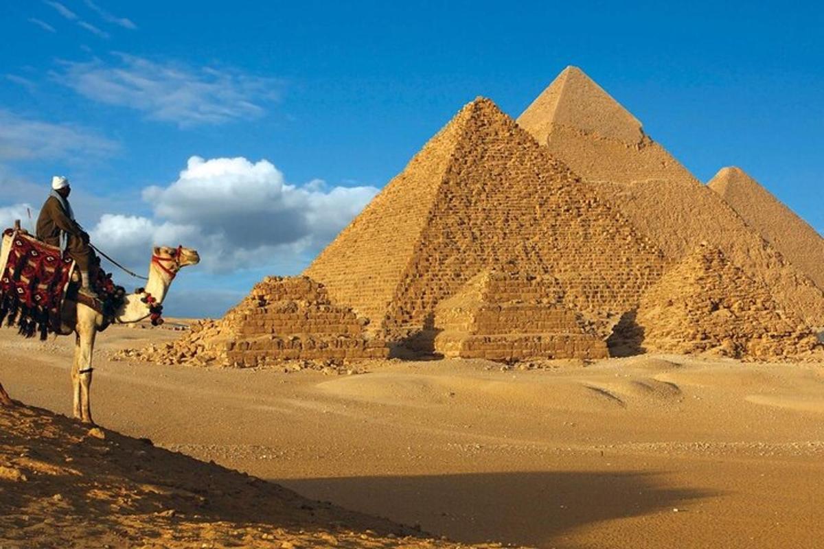 muž jedoucí na velbloudovi před pyramidami