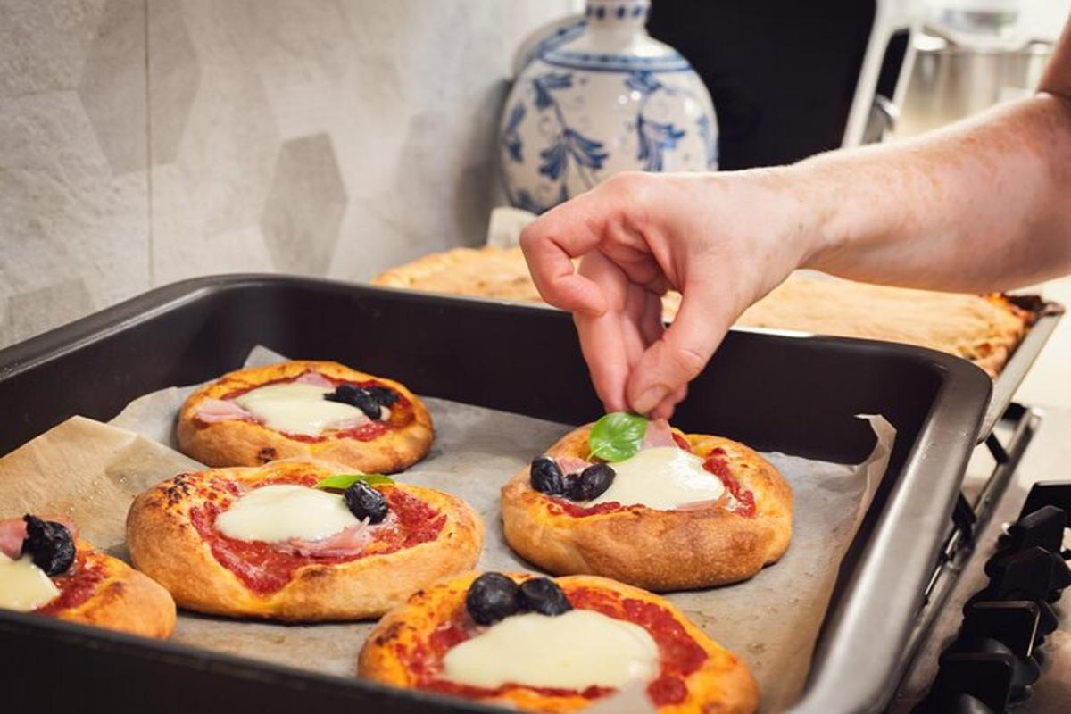 een persoon die naar een blad op een dienblad met minipizza's grijpt