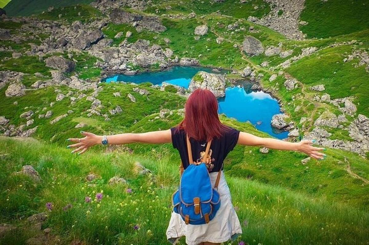 Una mujer con una mochila azul parada en una colina con los brazos extendidos.