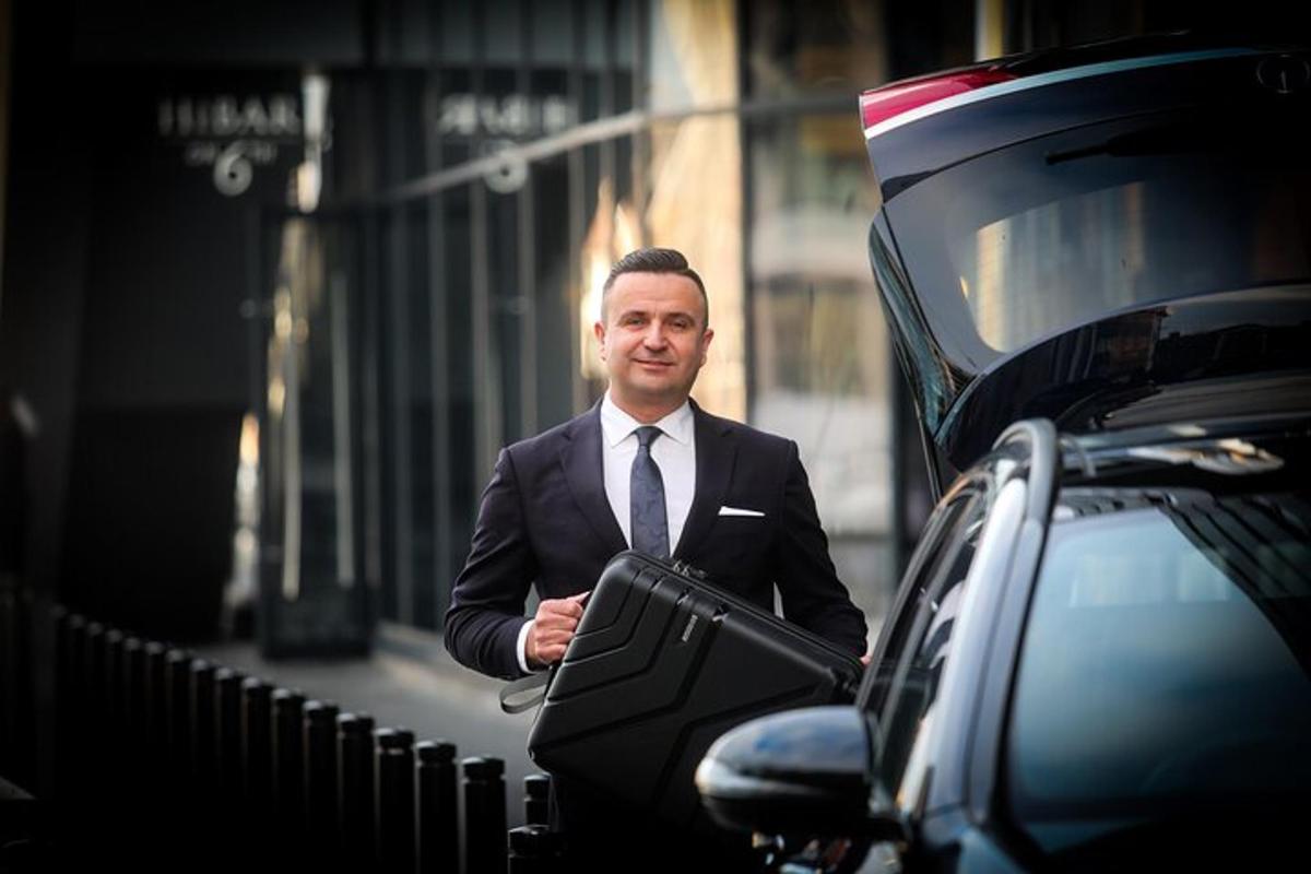 човек у оделу и кравати стоји поред аутомобила