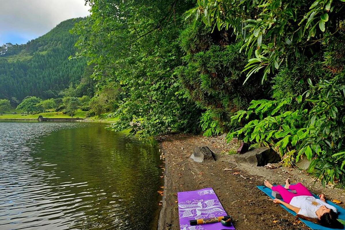 two people laying on towels on the shore of a lake