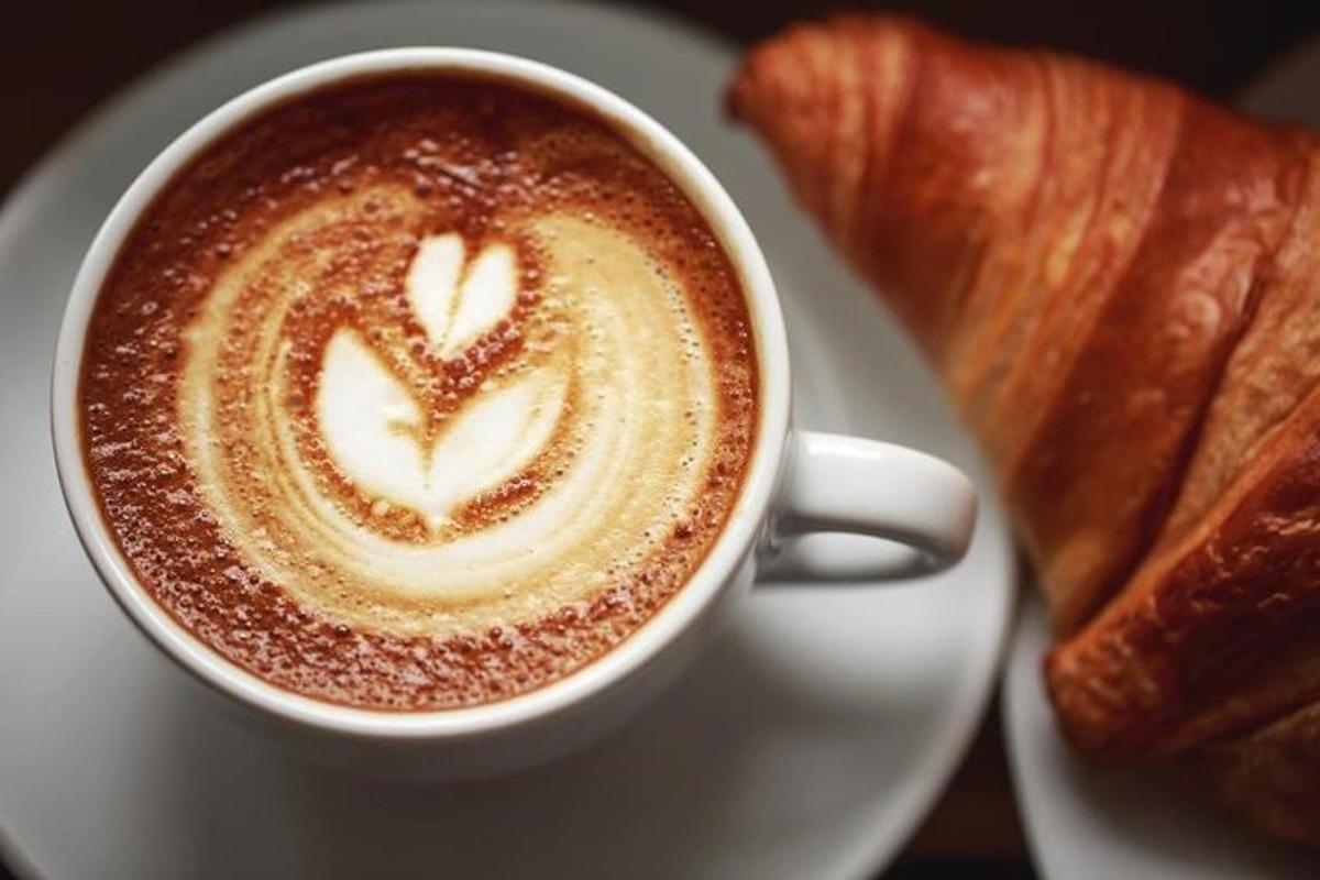 en kopp kaffe på en tallerken med en croissant