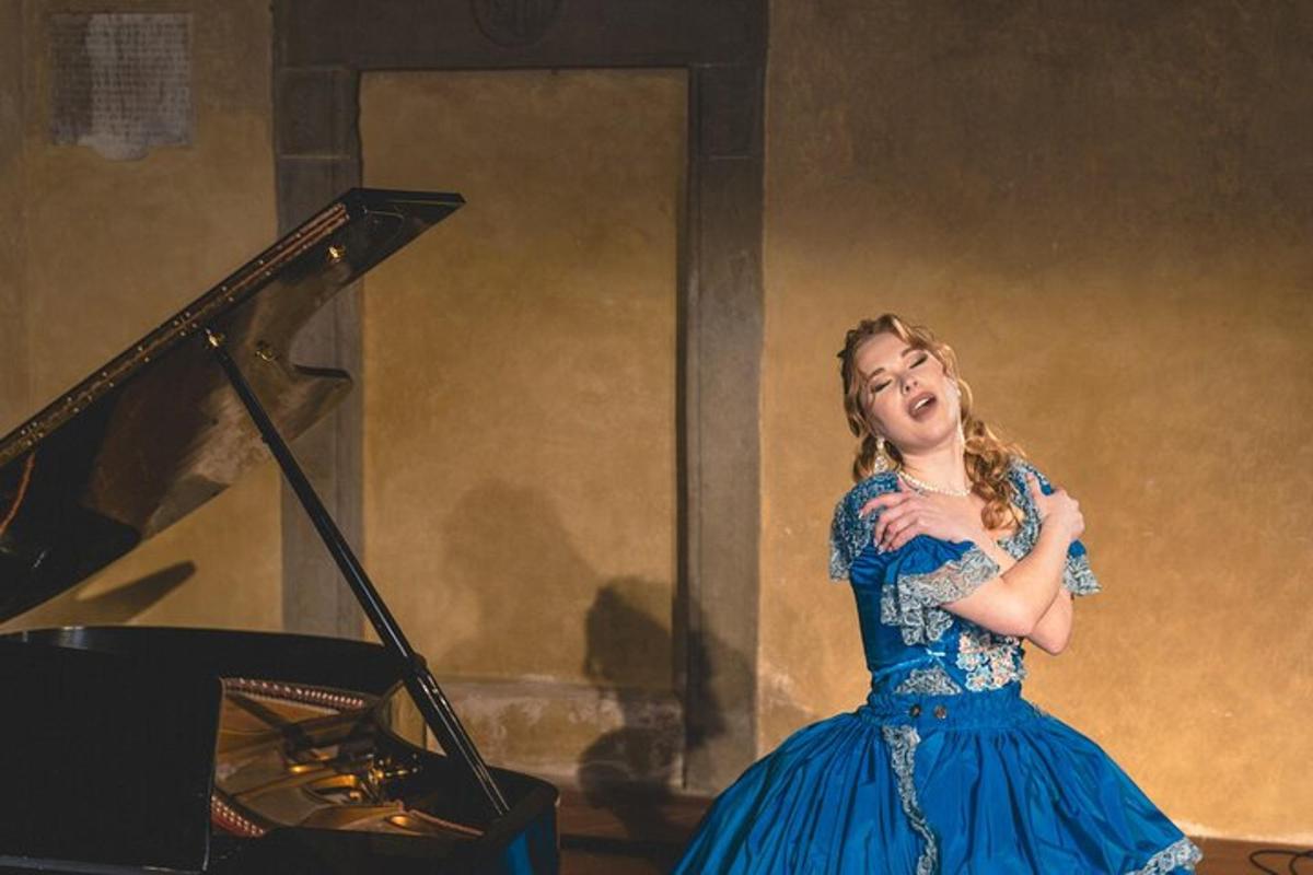 una dona amb un vestit blau dempeus al costat d'un piano