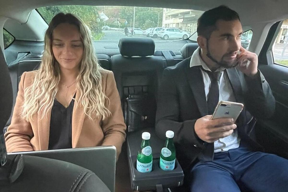 a man and a woman sitting in the back of a car looking at a tablet