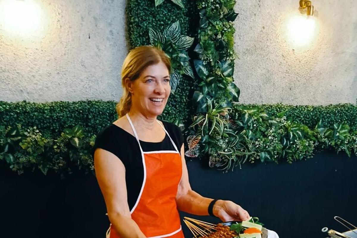 ženska v oranžnem predpasniku, ki drži krožnik hrane