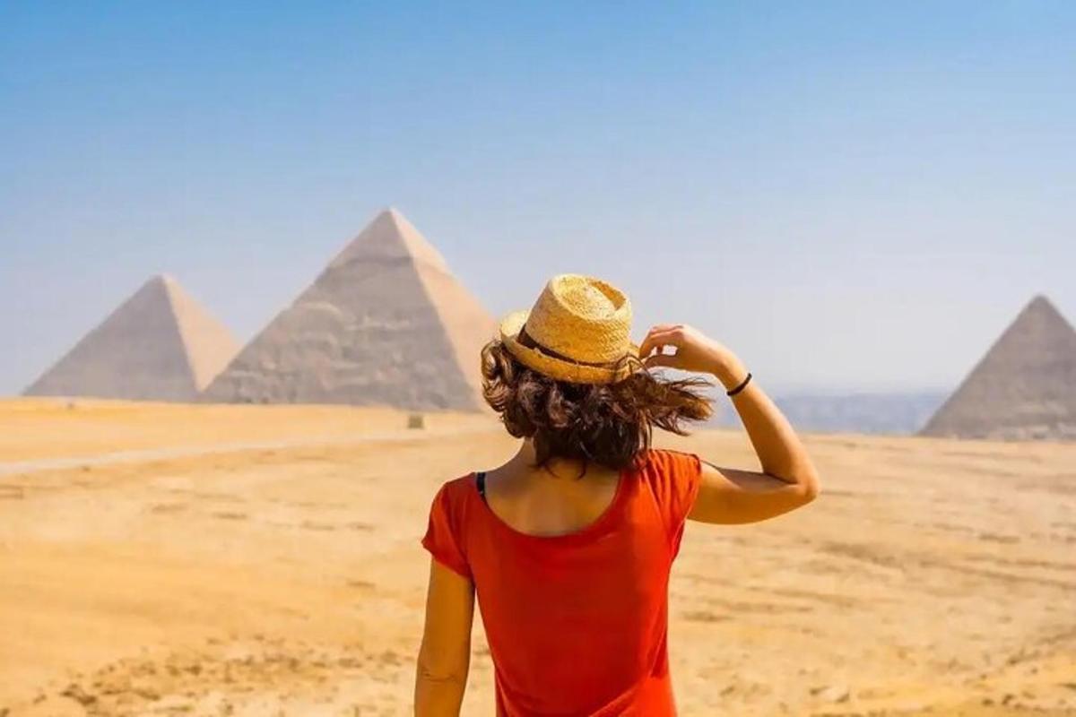 en kvinne i hatt som står foran pyramider