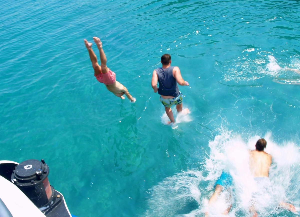 a group of people jumping off a boat in the water