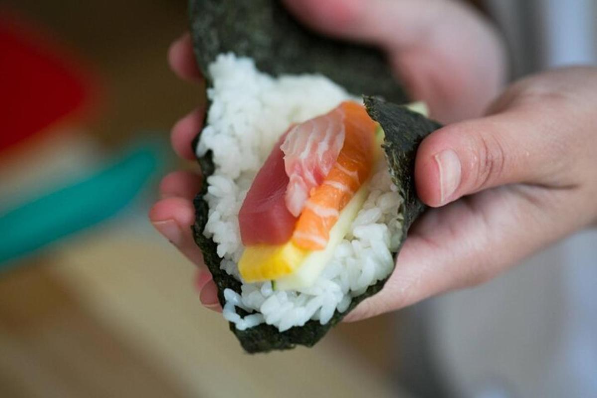 una persona che tiene in mano un pezzo di sushi con carne e riso