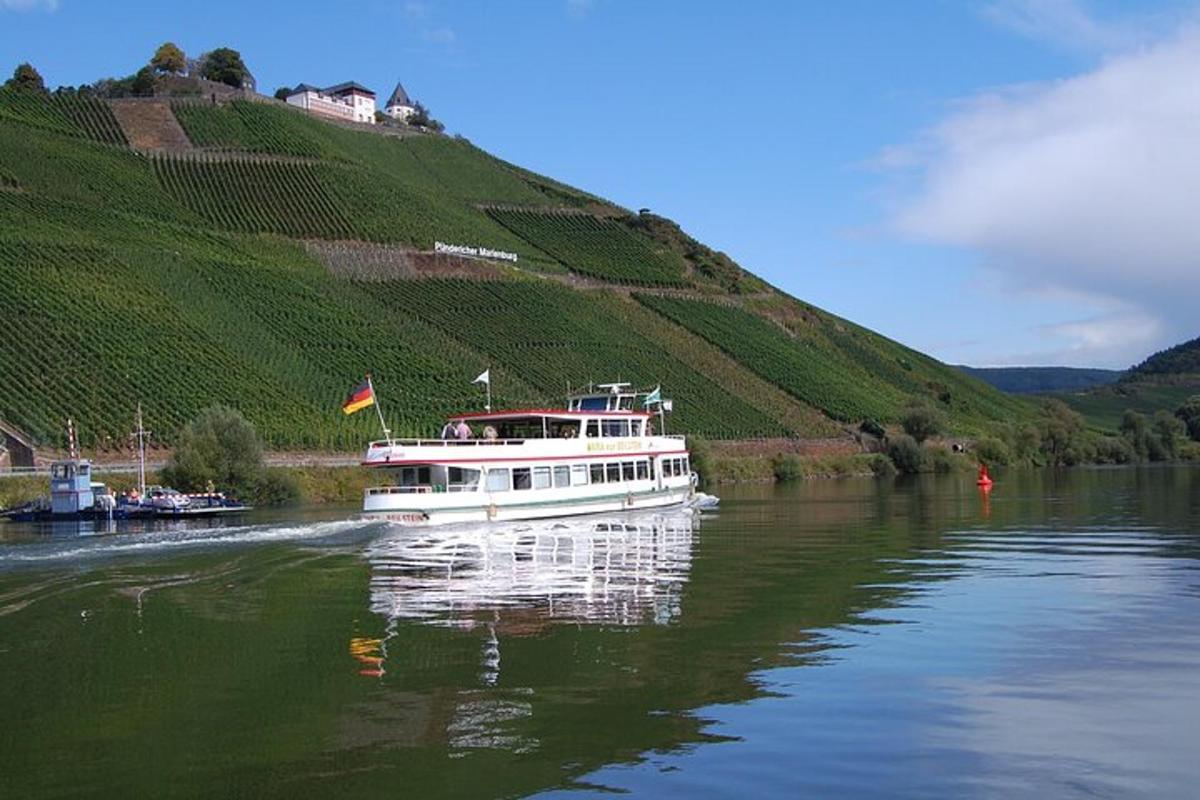 a white boat on a river next to a vineyard