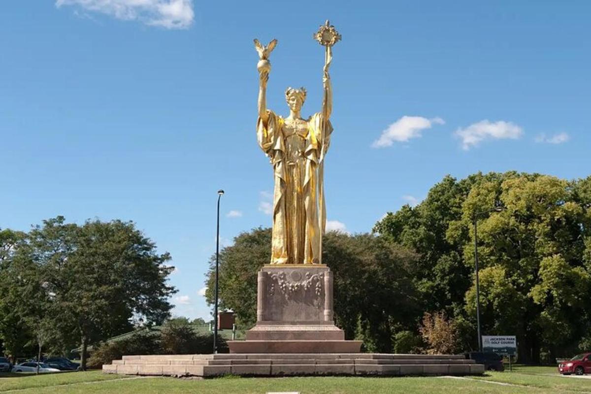 a gold statue in a park with a blue sky