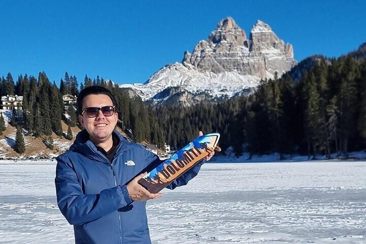 um homem segurando uma prancha de snowboard em frente a uma montanha