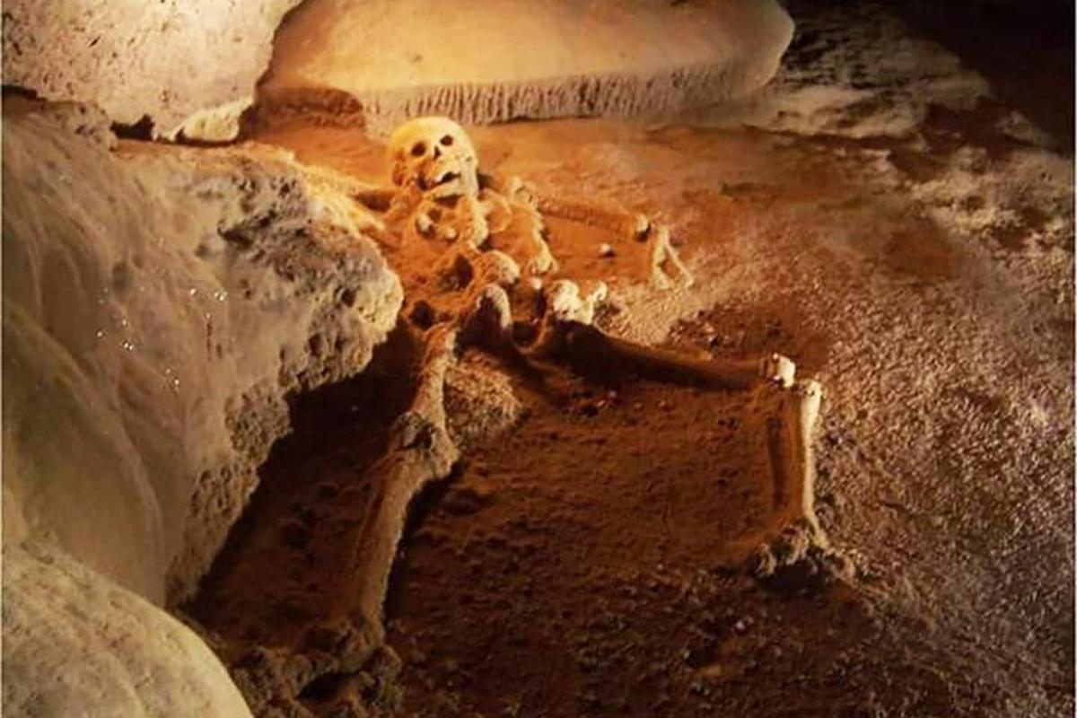 a skeleton sitting on the ground in a cave