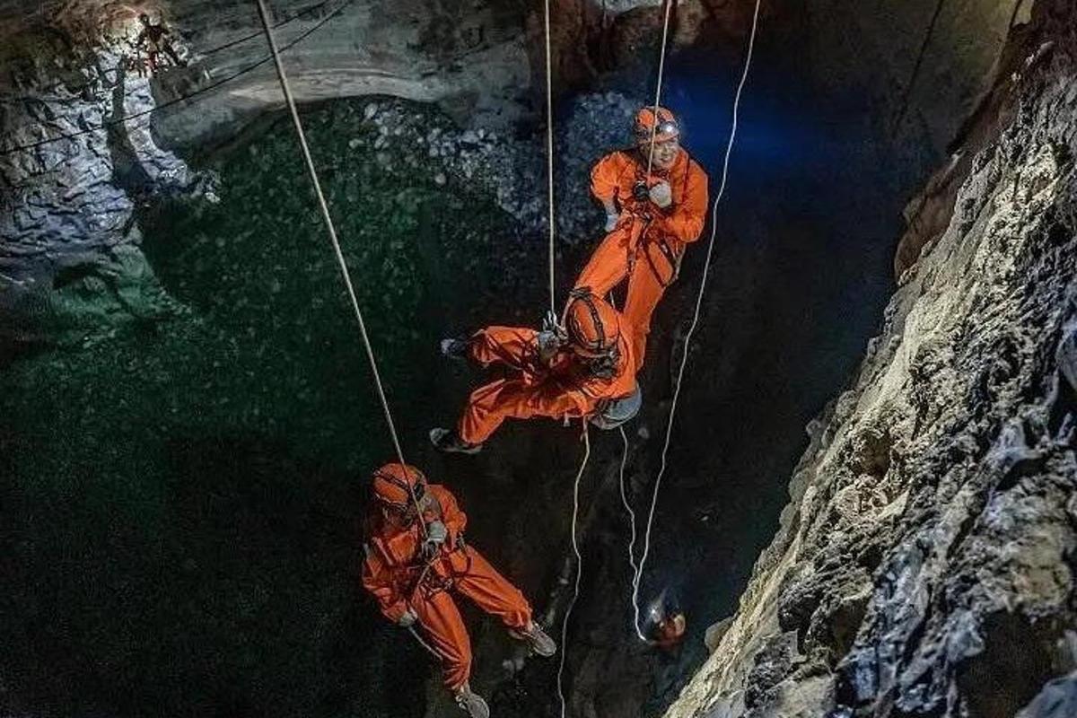 tiga lelaki berbaju oren sedang bertali dalam sebuah gua