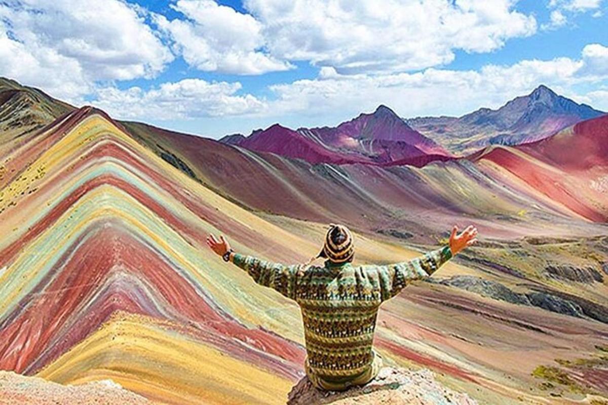 un uomo seduto su una roccia che guarda un dipinto di montagne