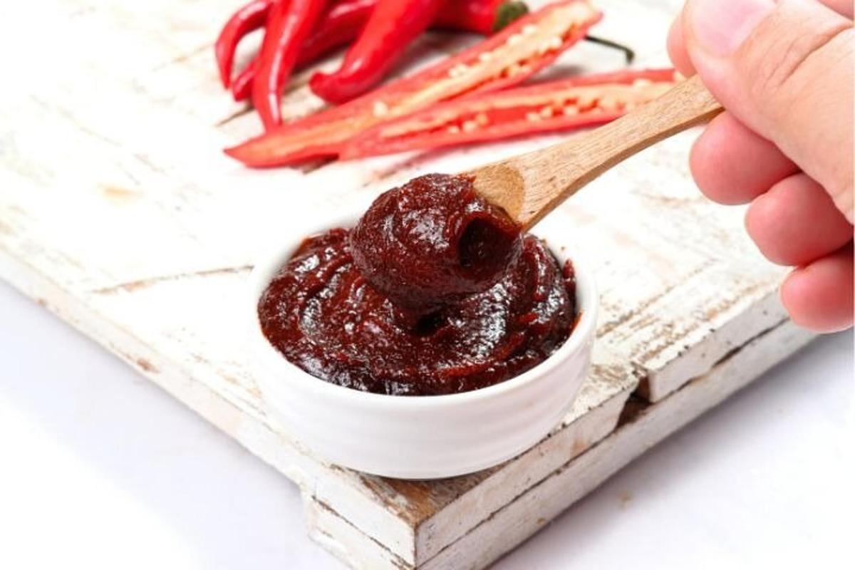 một người cầm một chiếc thìa gỗ đựng nước sốt trong bát
