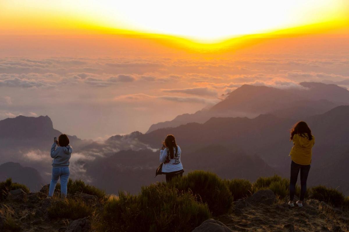 three women standing on top of a mountain at sunset