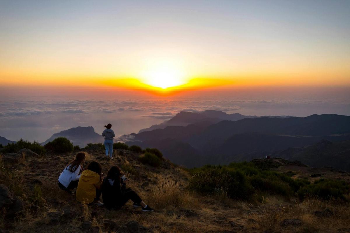 a group of people sitting on a hill watching the sunset
