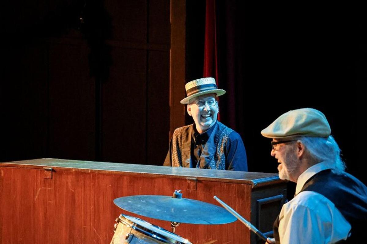 a man in a hat standing behind a table with a drummer