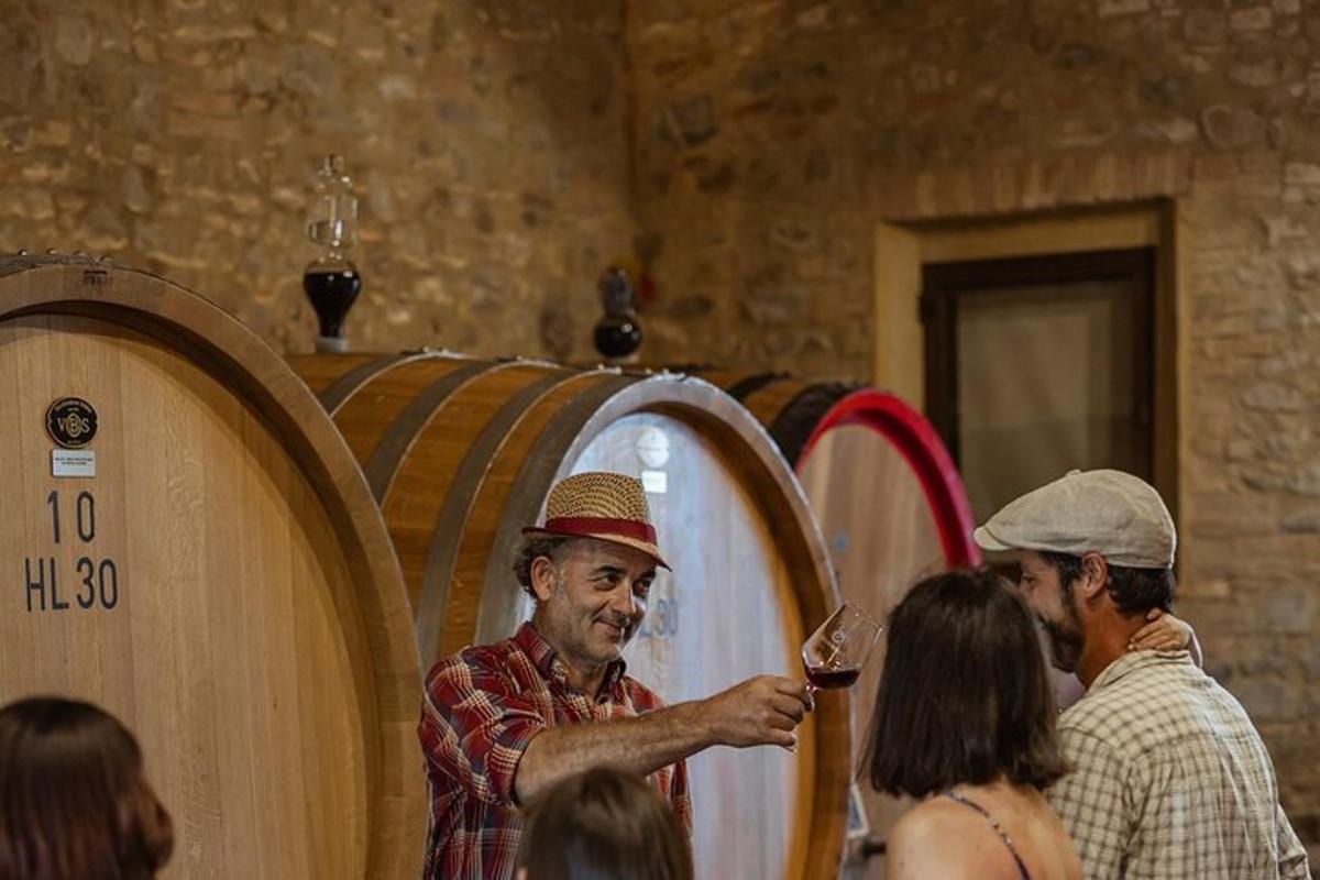 um homem segurando uma taça de vinho em frente aos barris