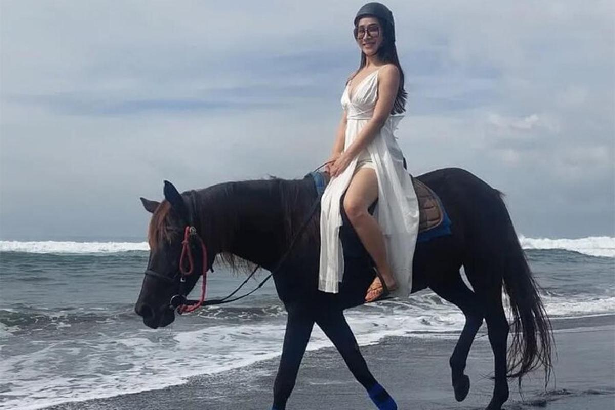 eine Frau in einem Kleid, die auf einem Pferd am Strand reitet