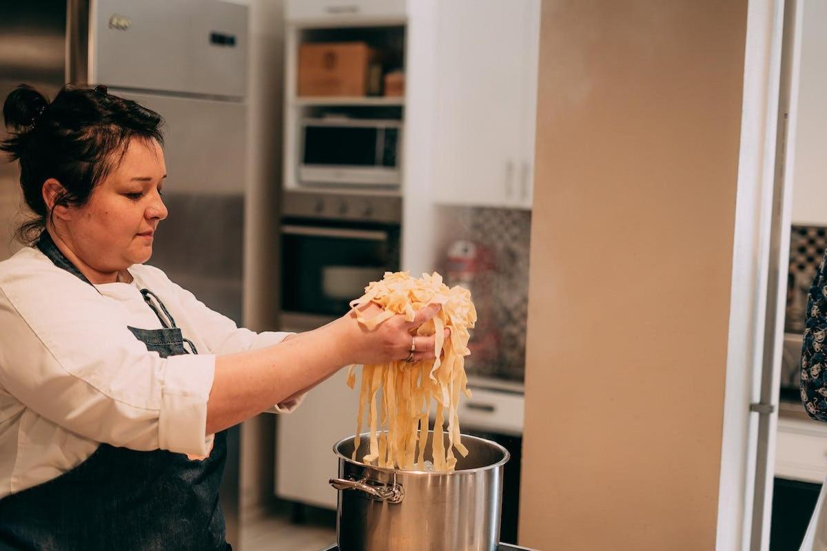 a woman in a kitchen holding a pot of spaghetti